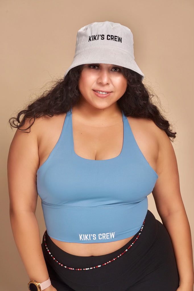 Model 2, female, wearing kiki's crew with corduroy bucket hat along with kiki's crew baby blue sports tank top