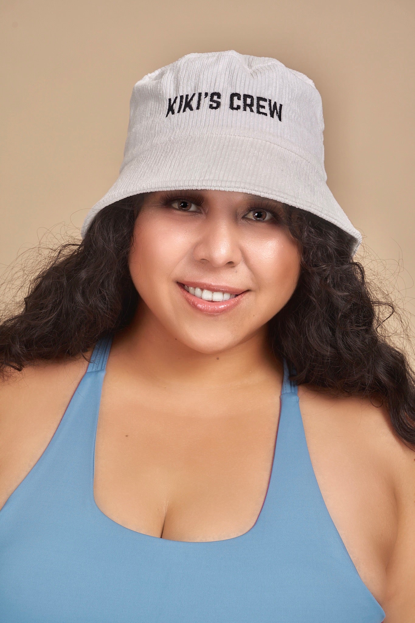 Model 2, female, wearing kiki's crew with corduroy bucket hat along with kiki's crew baby blue sports tank top