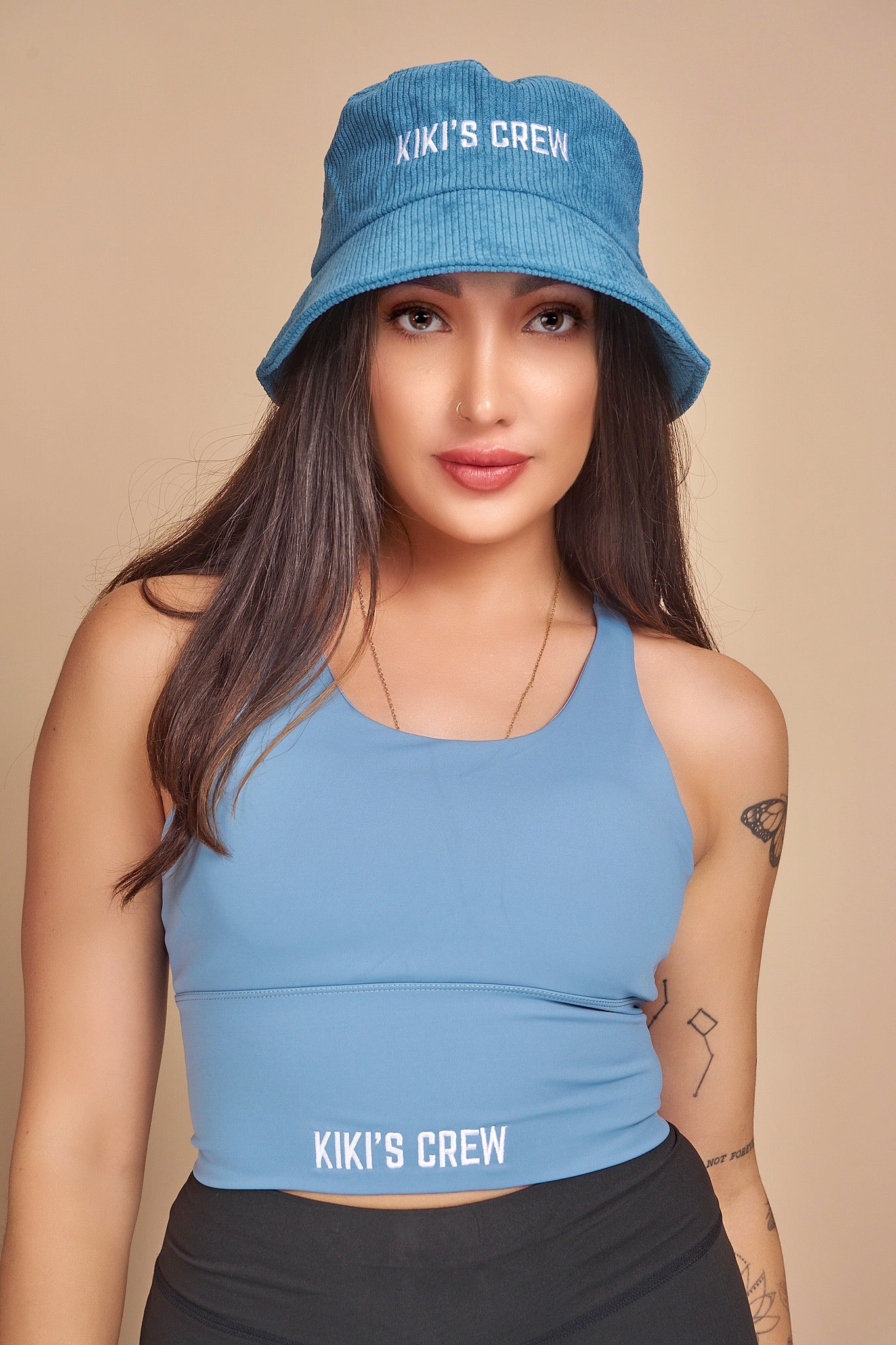 Model 4, female, wearing Kiki's Crew blue corduroy bucket hat along with kiki's crew baby blue sports tank top