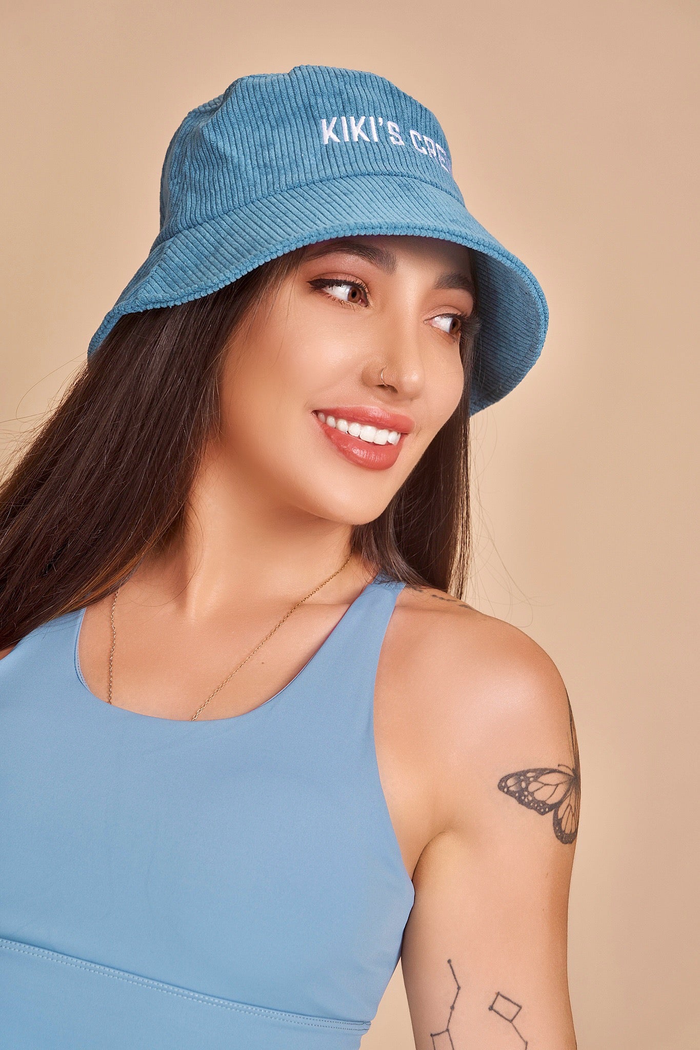 Model 4, female, wearing Kiki's Crew blue corduroy bucket hat along with kiki's crew baby blue sports tank top
