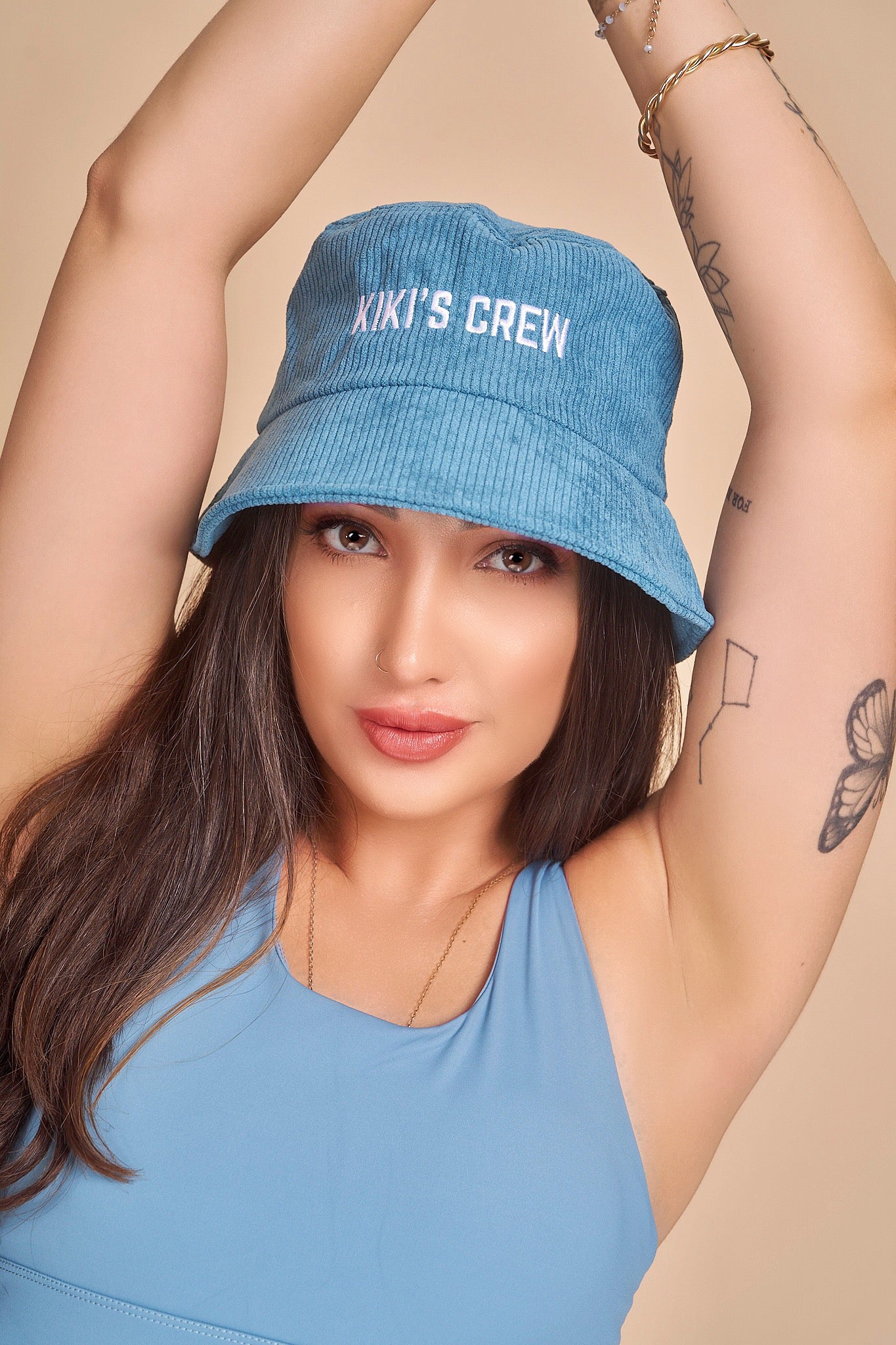 Model 4, female, wearing Kiki's Crew blue corduroy bucket hat along with kiki's crew baby blue sports tank top