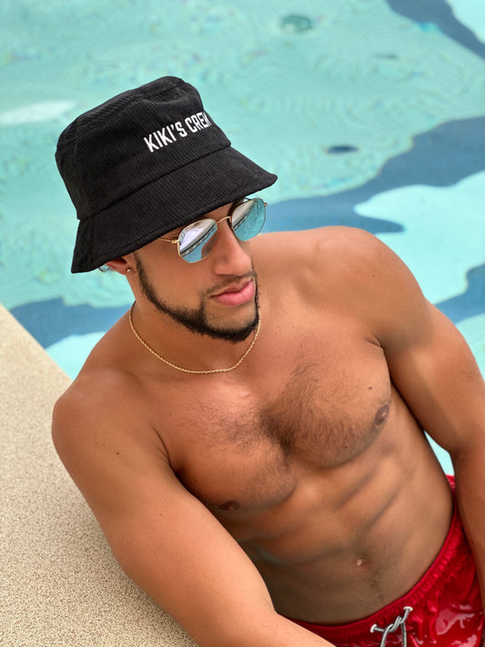 Model 1, male, at the pool wearing kiki's crew black corduroy bucket hat