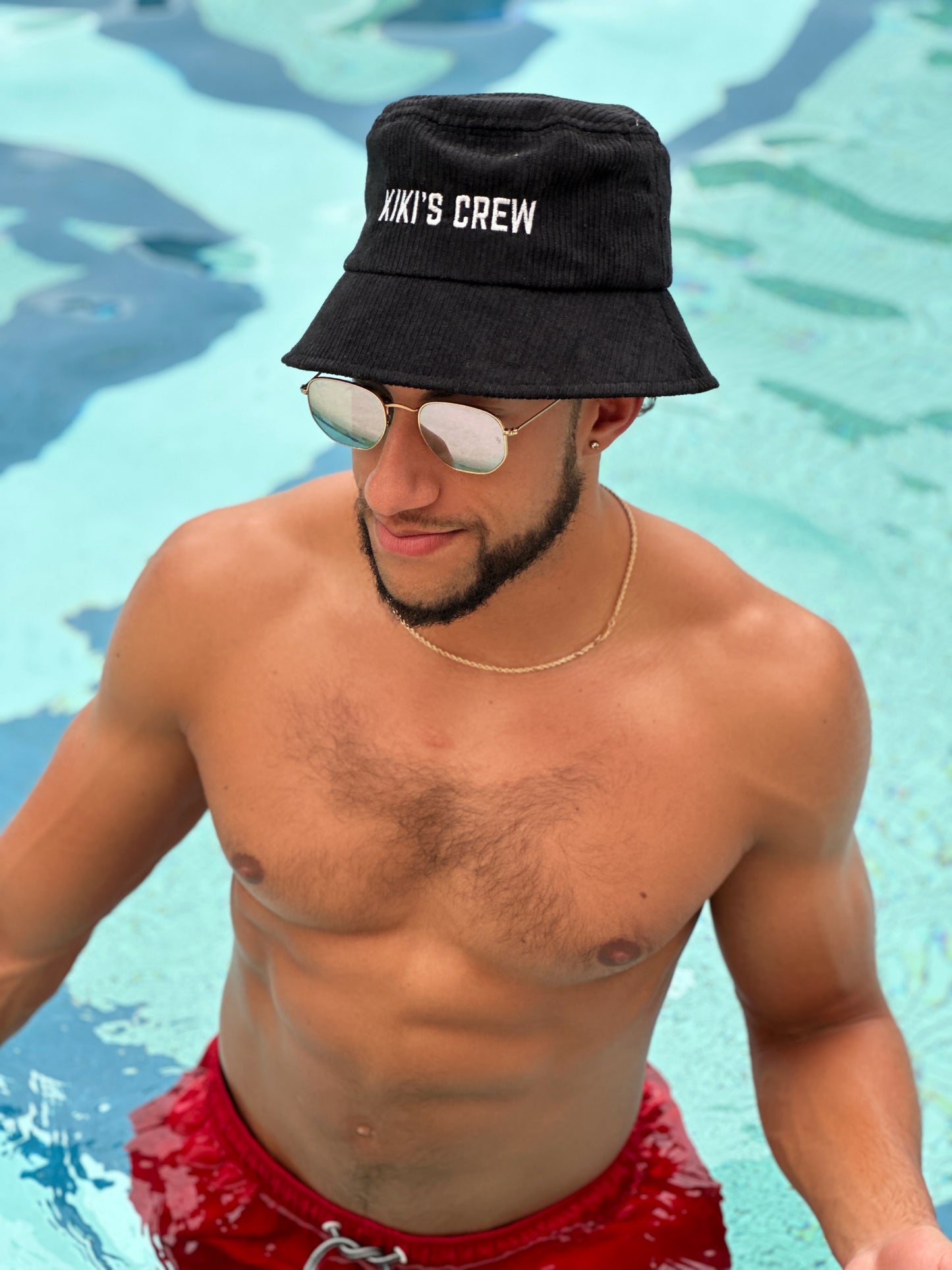 Model 1, male, at the pool wearing kiki's crew black corduroy bucket hat