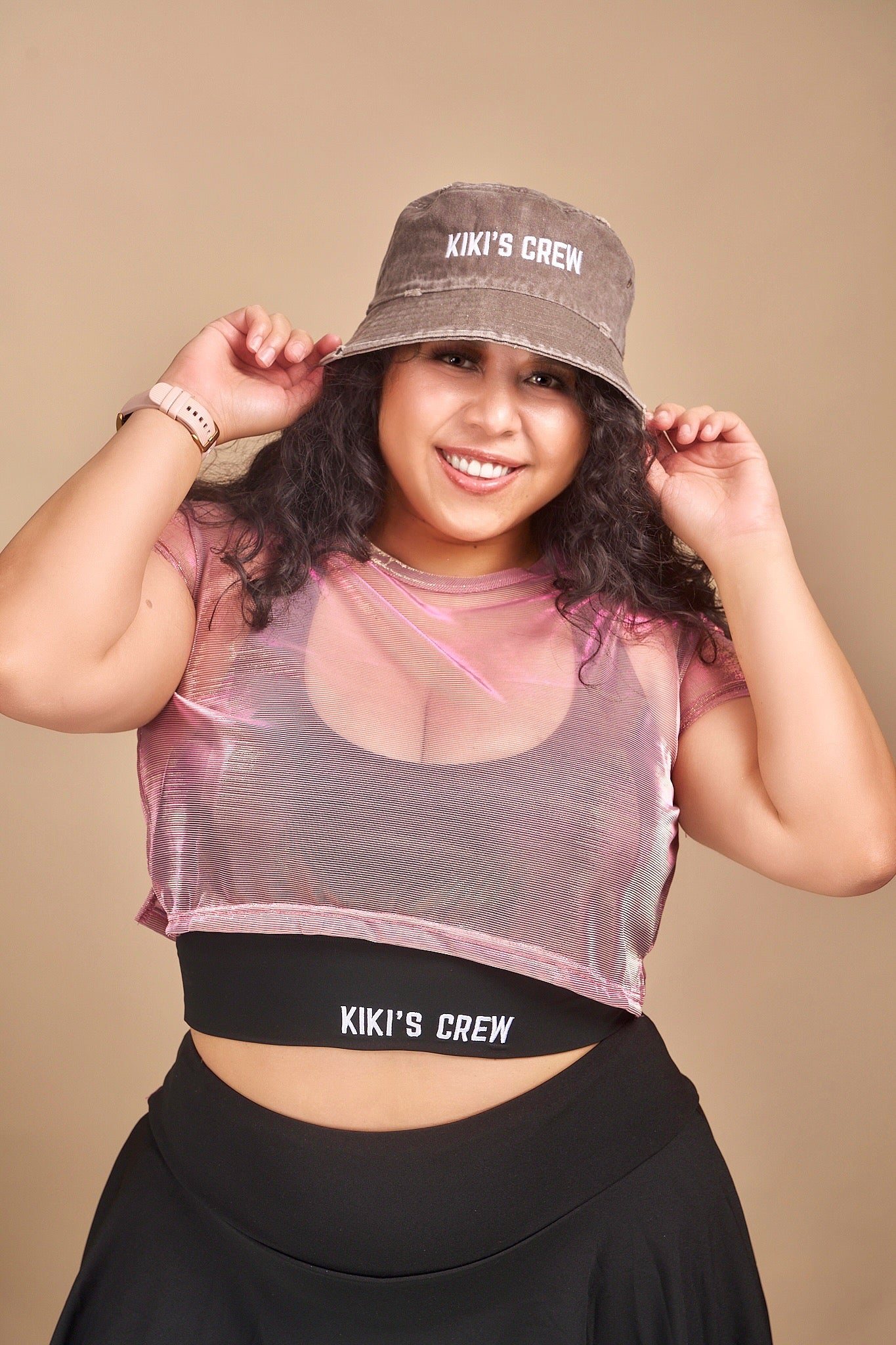 Female model wearing Kiki's crew brown vintage bucket hat along with kiki's crew pink metallic mesh top and kiki's crew black sports top size large and kiki's crew tennis skort size extra large