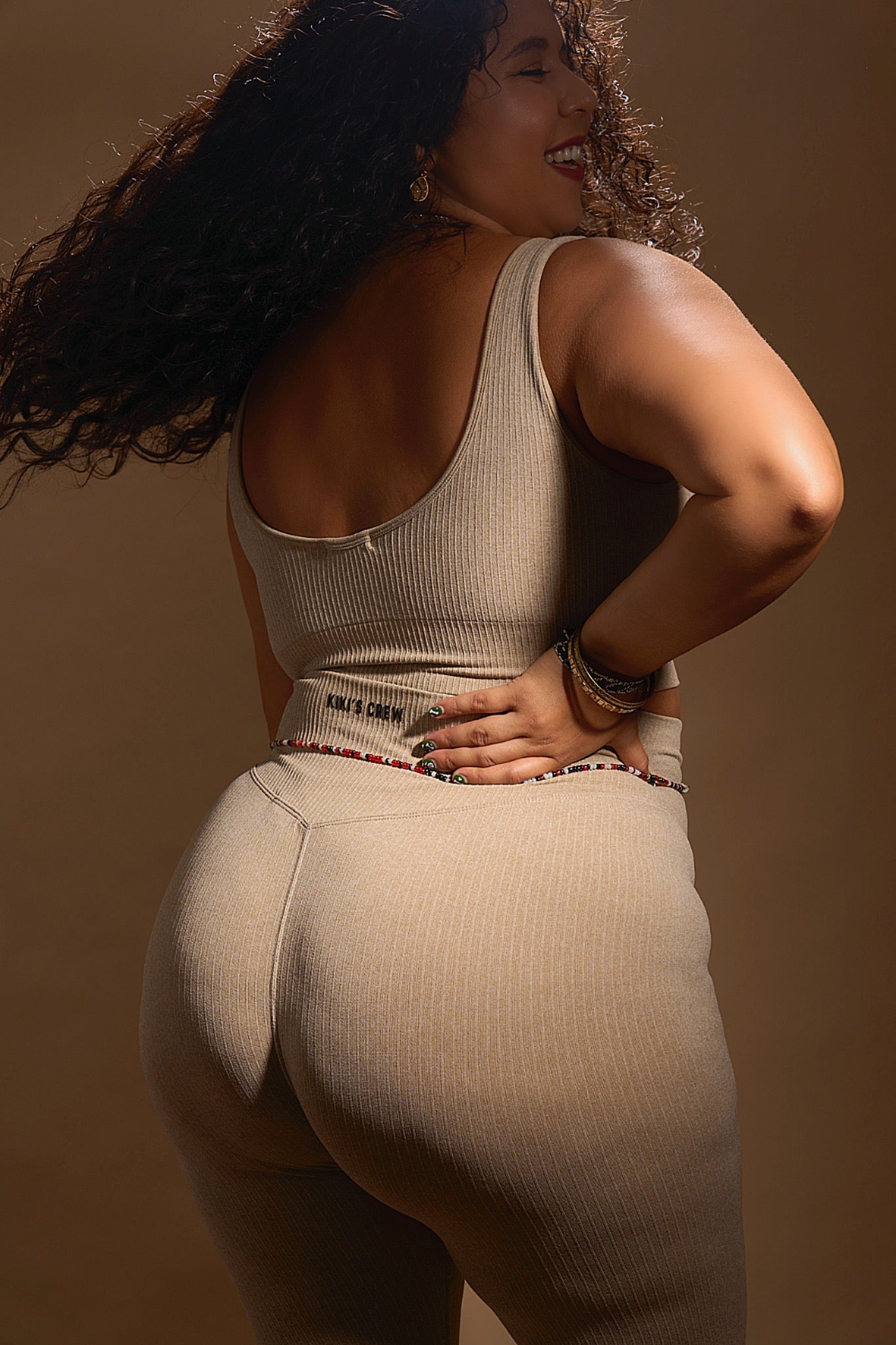 Model 2 wearing size large of kiki's crew matching sports top and leggings, color beige, showing the back of the set