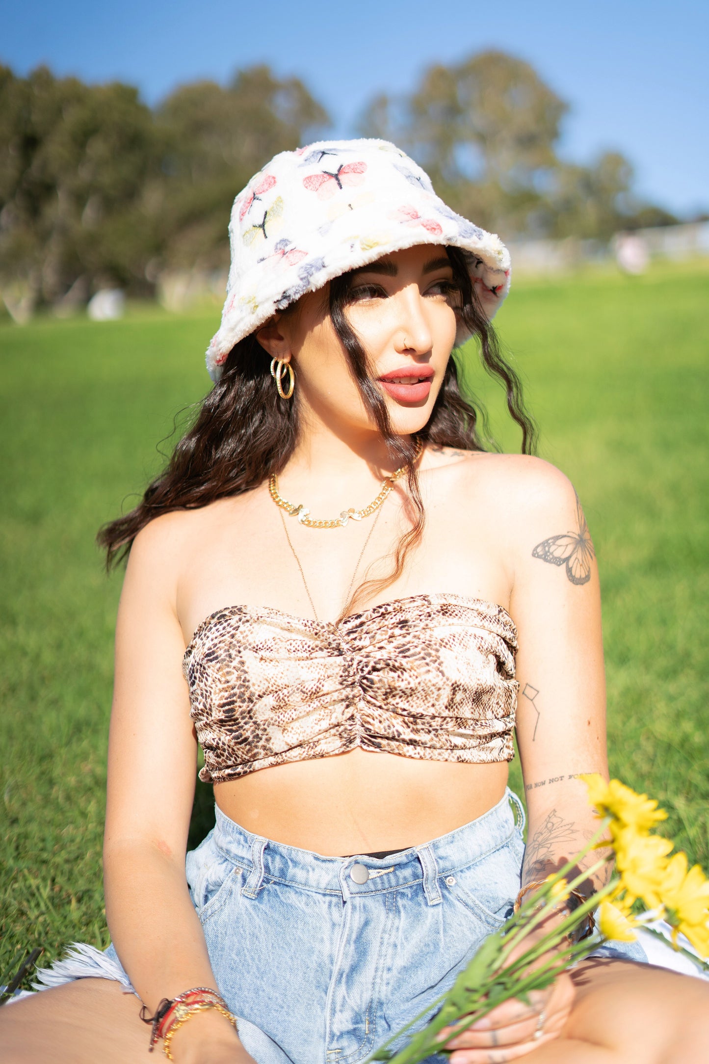 Kiki wearing a white fuzzy bucket hat at the park. It's design consists of different pastel colored butterflies, blue, red, yellow, and green