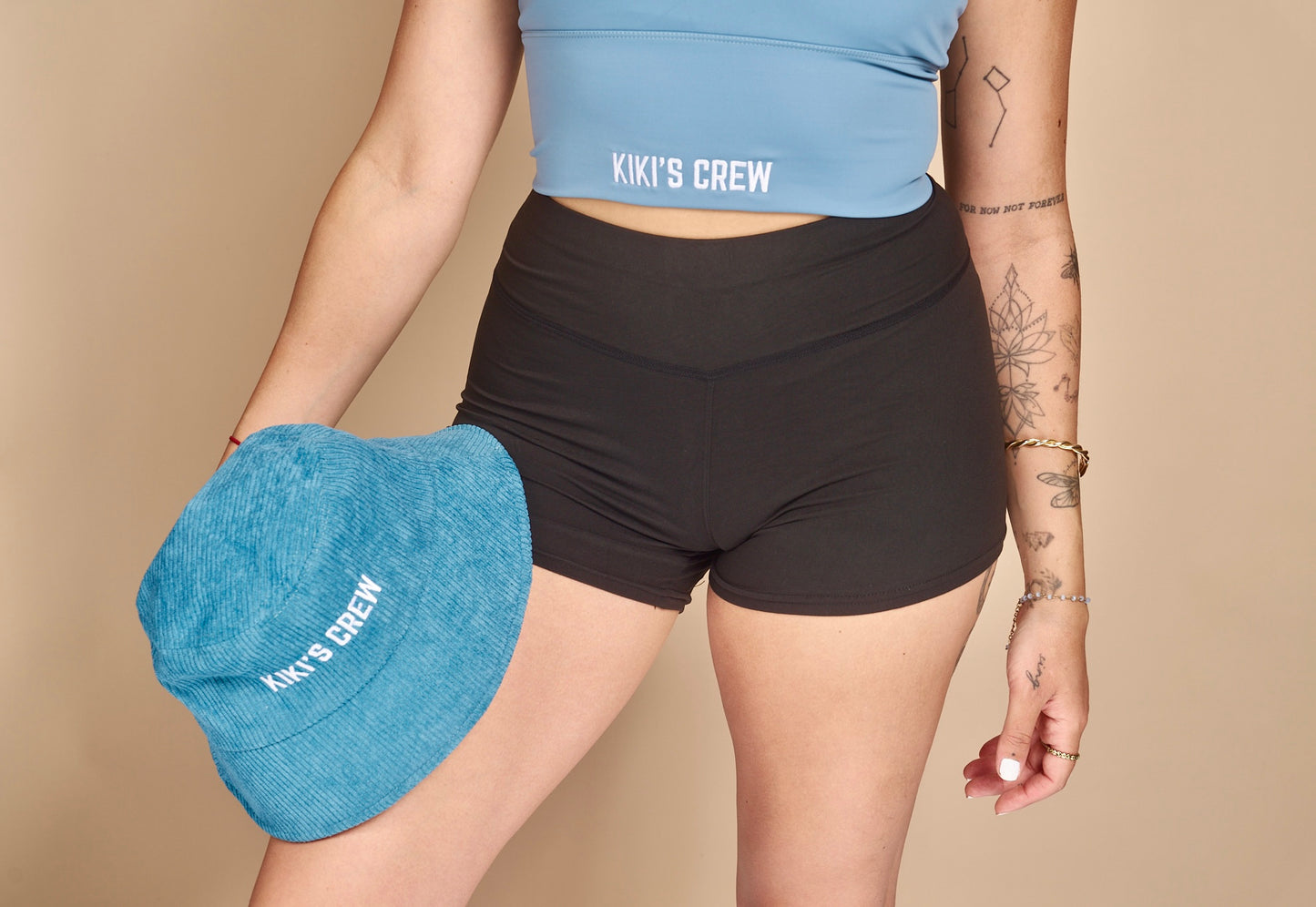 Model 1 wearing size small of the kiki's crew basic spandex shorts while holding Kiki's Crew Blue Corduroy bucket hat and wearing kiki's crew baby blue sports tank top