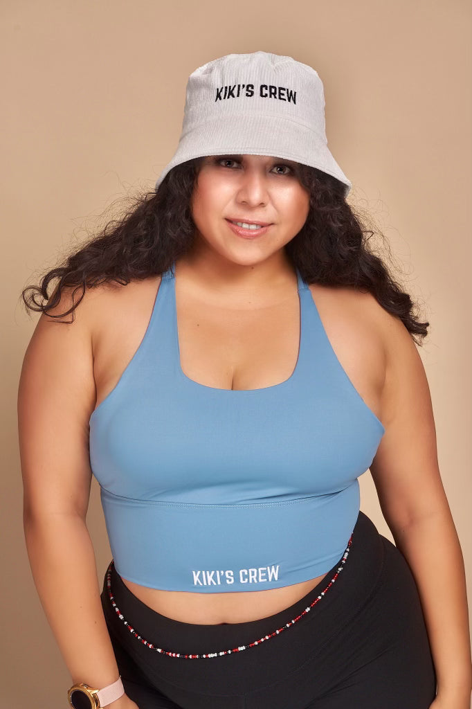 Model 2, female, wearing kiki's crew with corduroy bucket hat along with kiki's crew baby blue sports tank top 