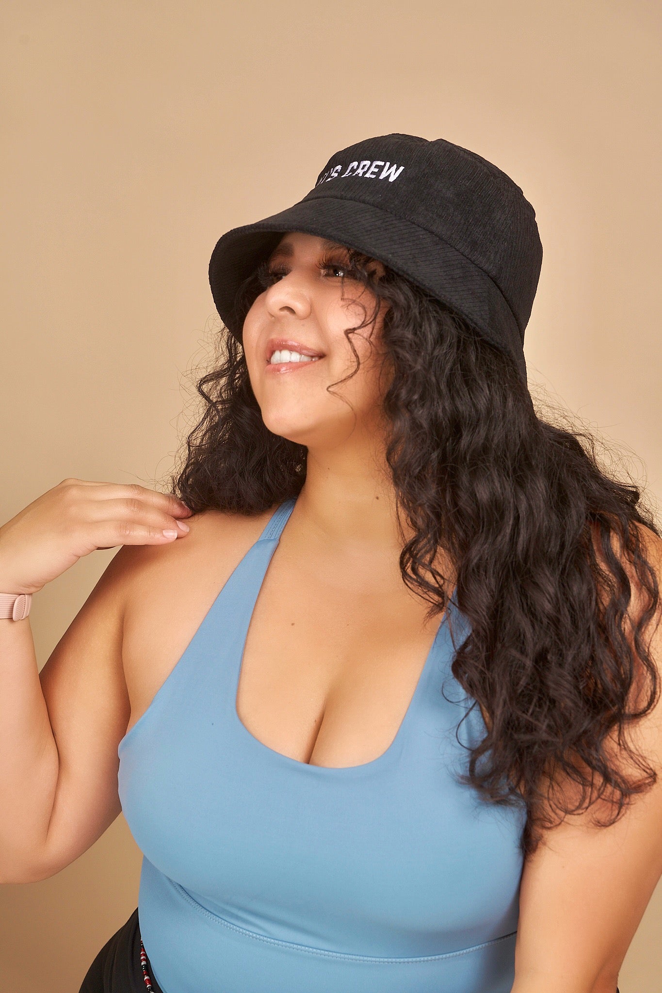 Model 2, female, wearing kiki's crew black corduroy bucket hat along with kiki's crew baby blue sports tank top 