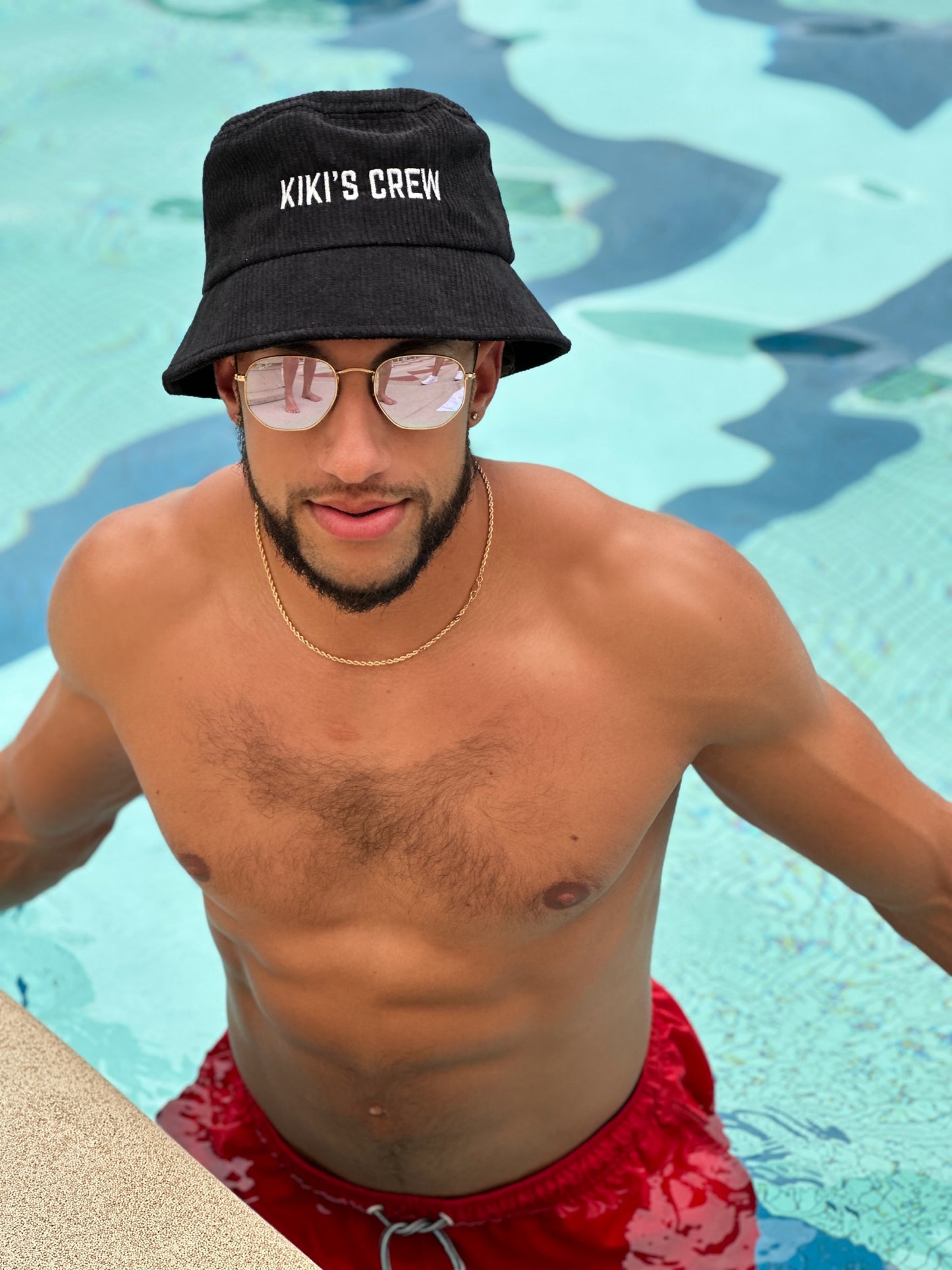 Model 1, male, at the pool wearing kiki's crew black corduroy bucket hat 