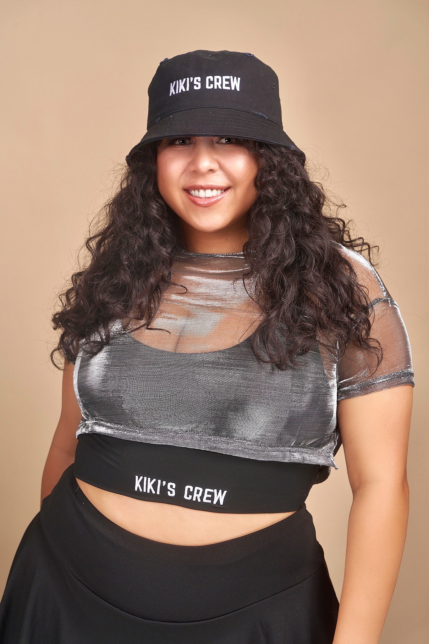 Female model wearing Kiki's crew black vintage bucket hat. this is a unisex product and accessory. she is also wearing kiki's crew metallic grey top with kiki's crew black sports bra size large and kiki's crew tennis skort size extra large 