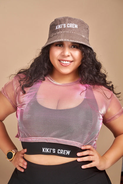 Female model wearing Kiki's crew brown vintage bucket hat along with kiki's crew pink metallic mesh top and kiki's crew black sports top size large and kiki's crew tennis skort size extra large 