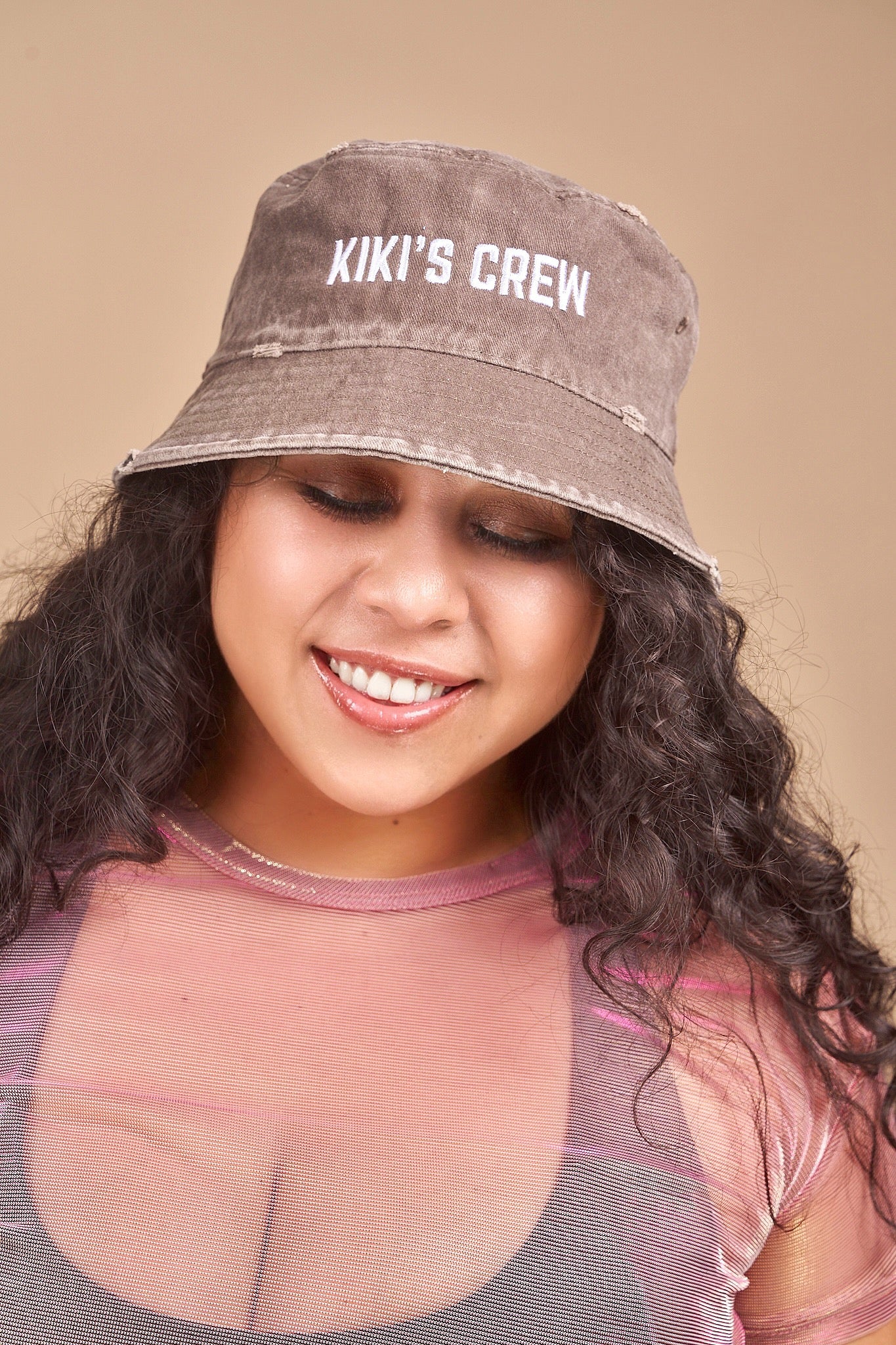 Female model wearing Kiki's crew brown vintage bucket hat along with kiki's crew pink metallic mesh top and kiki's crew black sports top size large