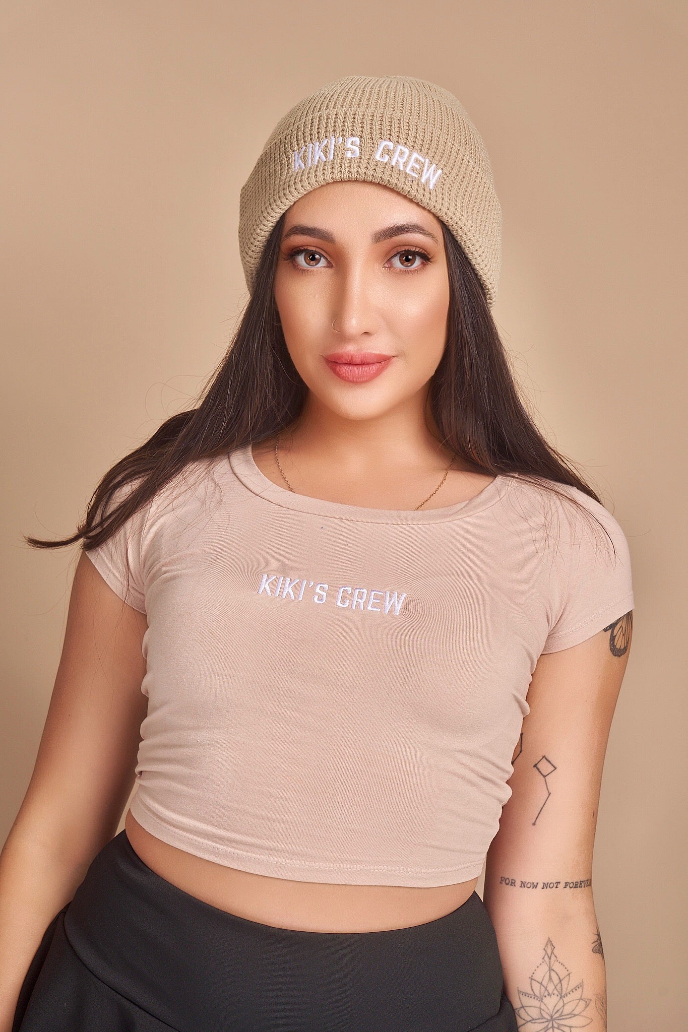 Model 1 is wearing a beige kiki's crew beanie. beanies are one size fits all and unisex. she is also wearing a size small kiki's crew t-shirt along with a kiki's crew size small tennis skort