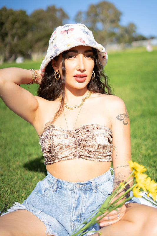 Kiki wearing a white fuzzy bucket hat at the park. It's design consists of different pastel colored butterflies, blue, red, yellow, and green 