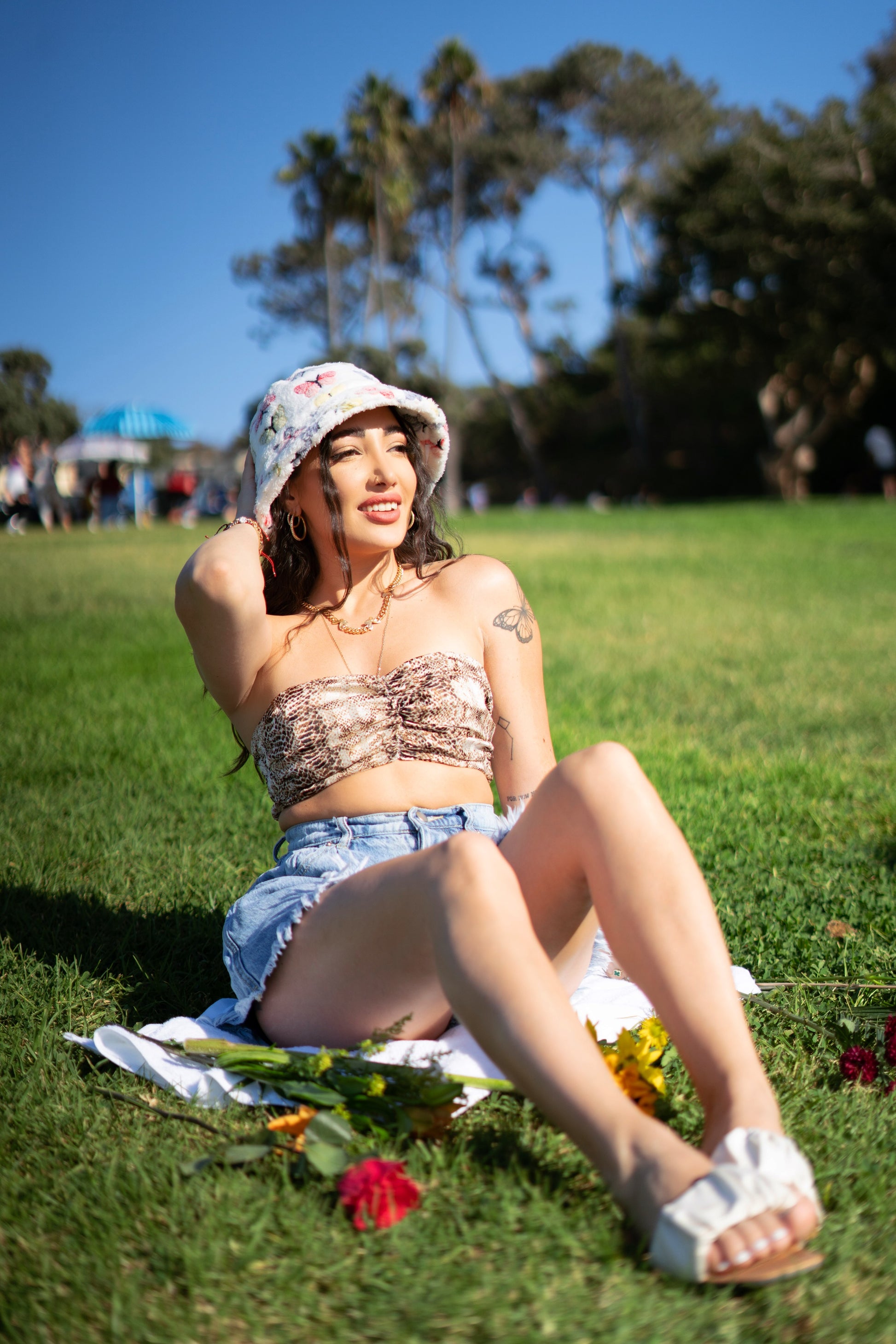 Kiki wearing a white fuzzy bucket hat at the park. It's design consists of different pastel colored butterflies, blue, red, yellow, and green 