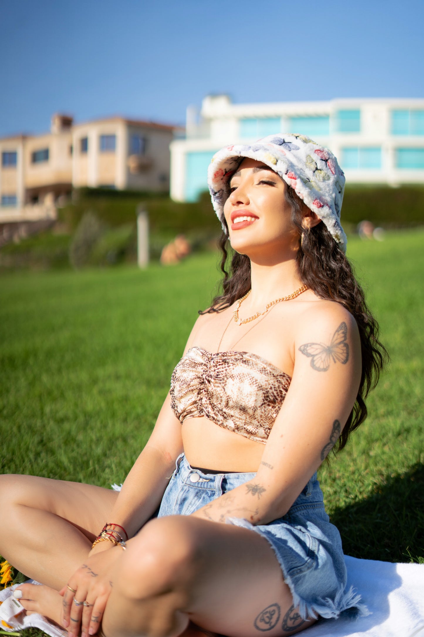 Kiki wearing a white fuzzy bucket hat at the park. It's design consists of different pastel colored butterflies, blue, red, yellow, and green 